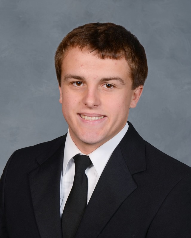 young man smiles wearing a black suit and tie